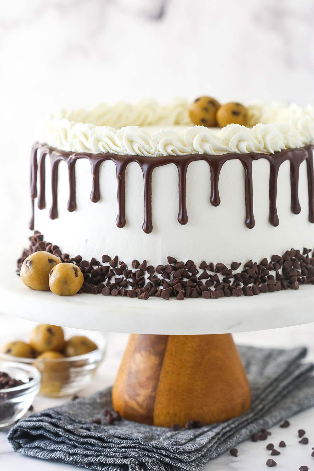 Ice cream cake on a cake stand near cookie dough and chocolate chips.