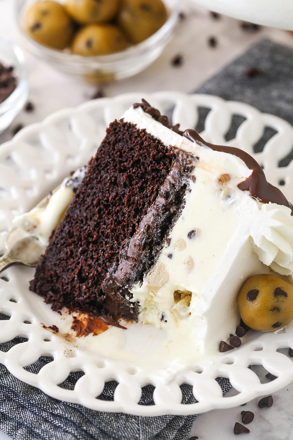 Chocolate cake, ice cream, fudgy chocolate, cookie crunchies, and a rich chocolate ganache make up this decadent ice cream cake. A slice of ice cream cake on a plate with. bite taken out of it.
