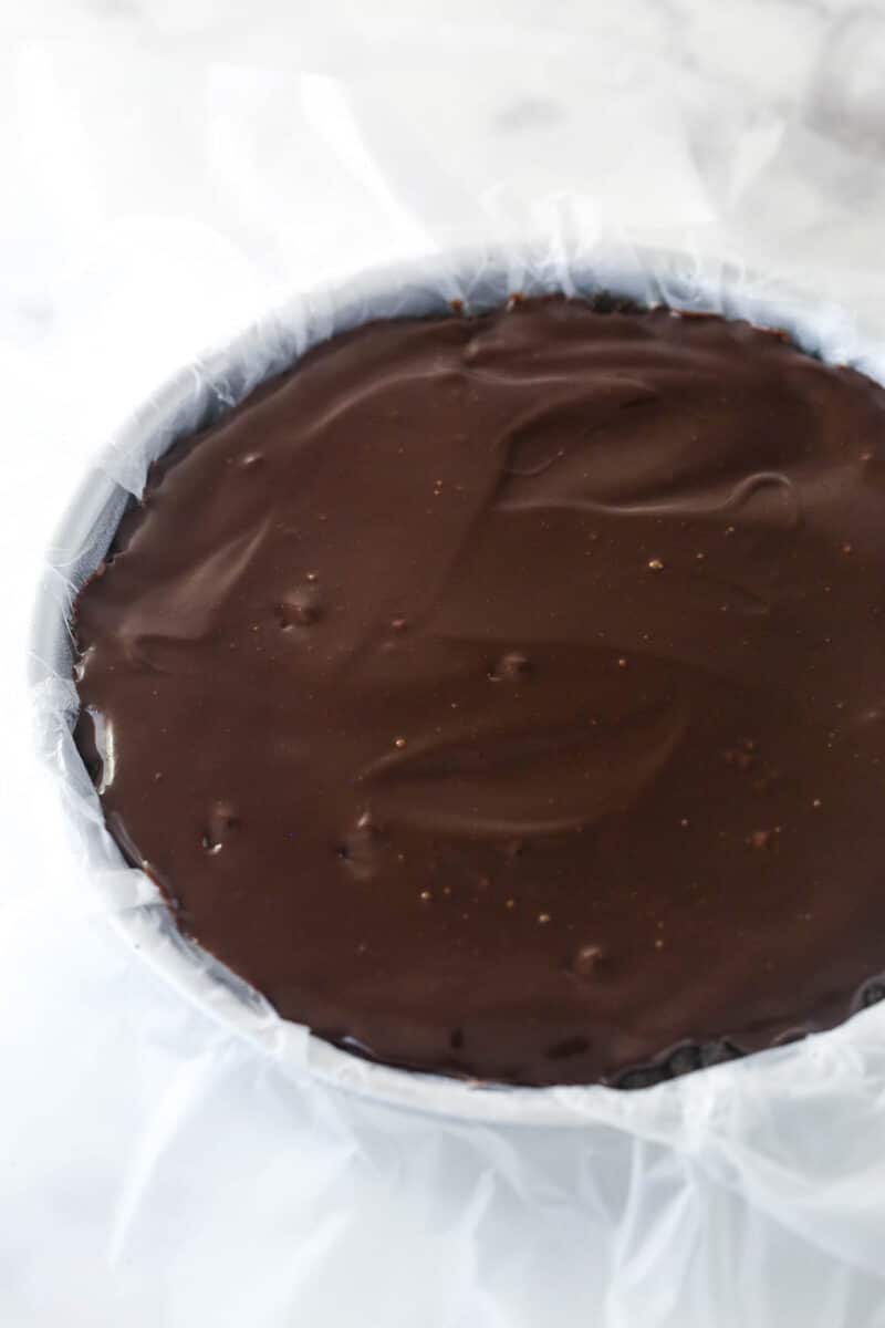Chocolate fudge layer over ice cream layer in a cake pan lined with clear wrap.