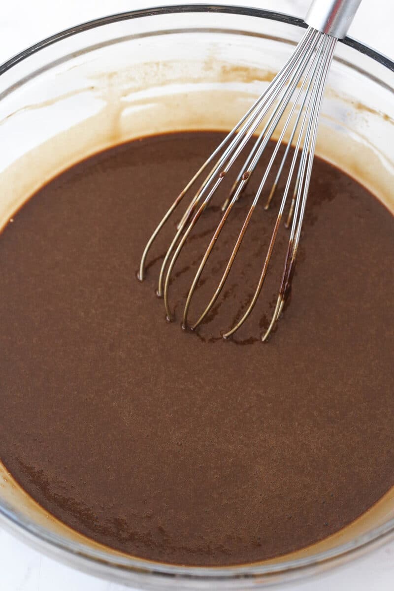 Chocolate cake batter in a mixing bowl with a whisk after adding hot water.