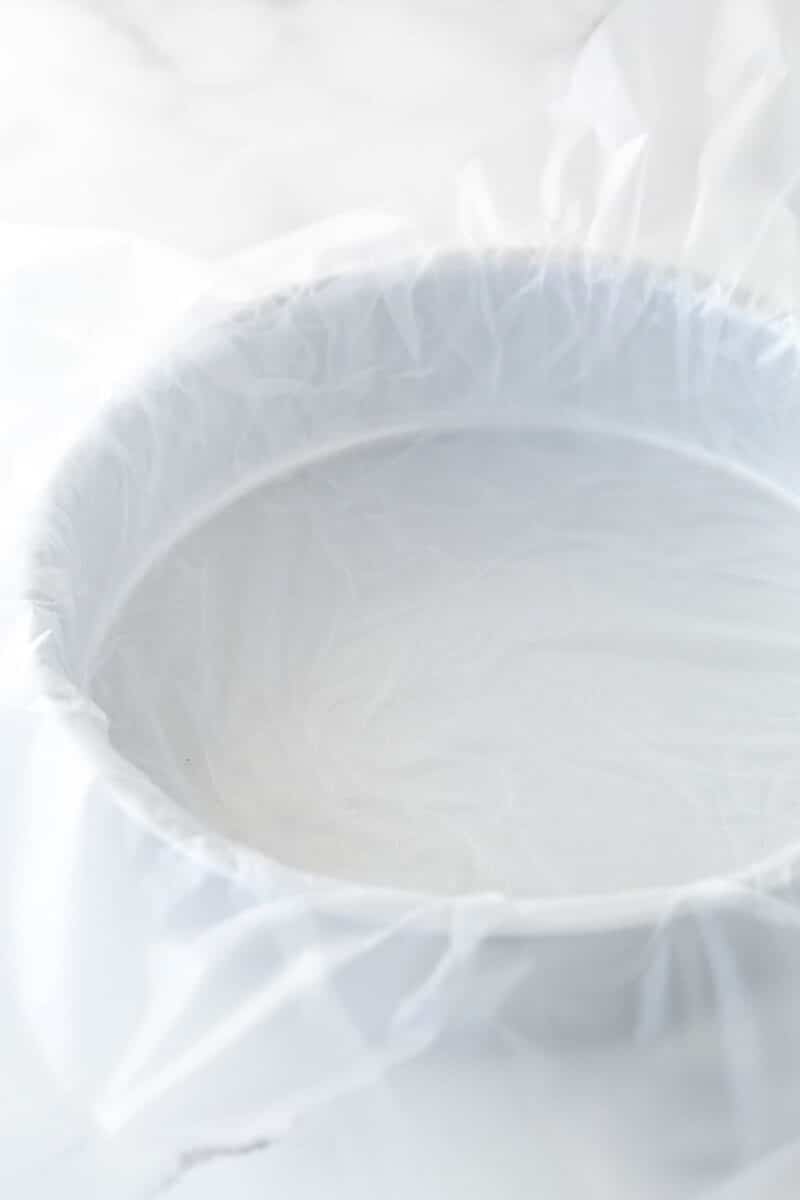A cake pan lined with clear wrap.