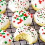 Italian Ricotta Cookies with red, green and white sprinkles spread over a metal cooling rack with one cookie missing a bite