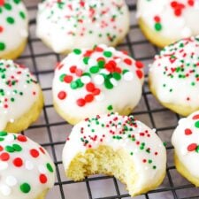Italian Ricotta Cookies with red, green and white sprinkles spread over a metal cooling rack with one cookie missing a bite