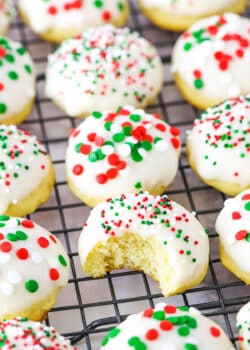 Italian Ricotta Cookies with red, green and white sprinkles spread over a metal cooling rack with one cookie missing a bite