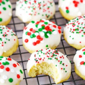 Italian Ricotta Cookies with red, green and white sprinkles spread over a metal cooling rack with one cookie missing a bite