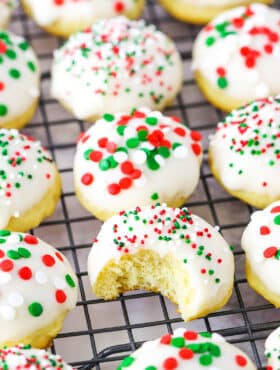 Italian Ricotta Cookies with red, green and white sprinkles spread over a metal cooling rack with one cookie missing a bite