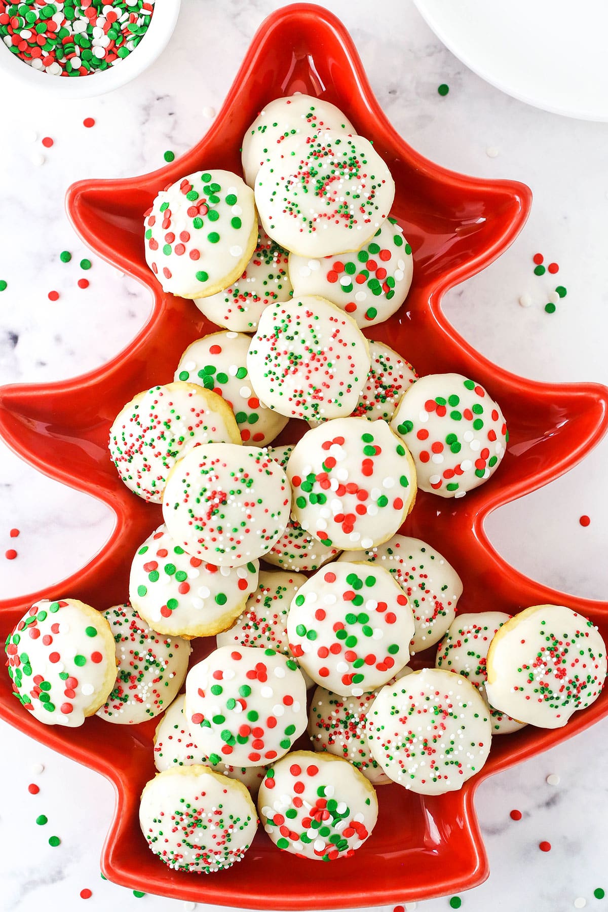 Italian Ricotta Cookies with red, green and white sprinkles layered in a red Christmas Tree shaped platter.