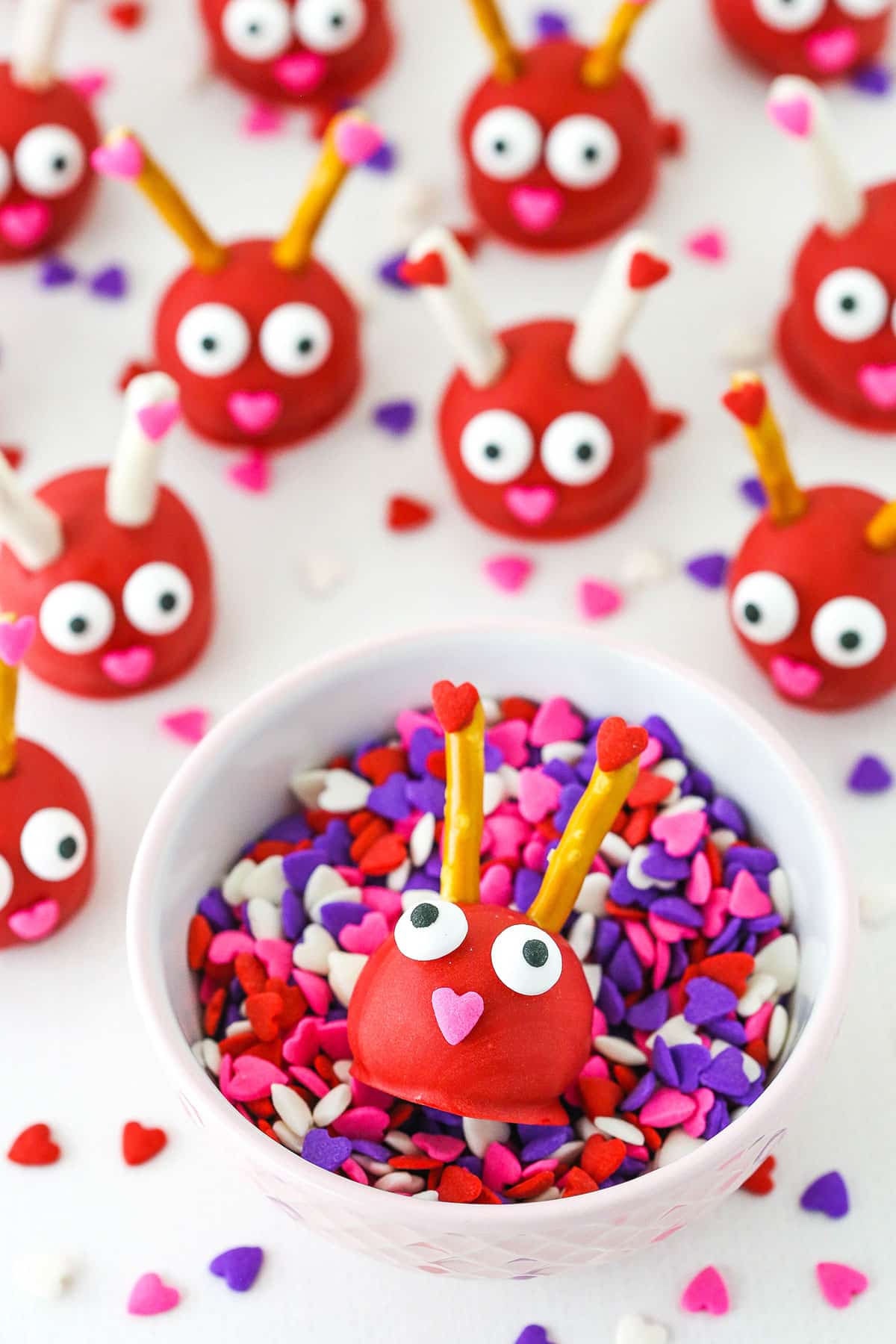 Love Bug Oreo Cookie Balls with pretzel sticks for feelers and heart noses displayed on a white marble table top