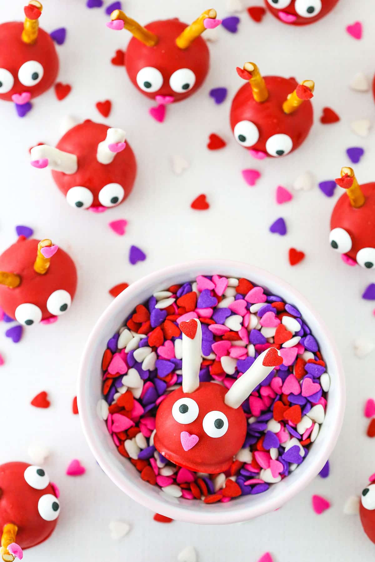 Love Bug Oreo Cookie Ball in a white bowl full of heart shaped sprinkles with more Love Bug Oreo Cookie Balls in the background