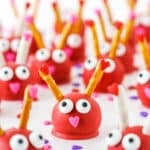 Love Bug Oreo Cookie Balls with pretzel sticks for feelers and heart noses displayed on a white marble table top