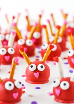 Love Bug Oreo Cookie Balls with pretzel sticks for feelers and heart noses displayed on a white marble table top