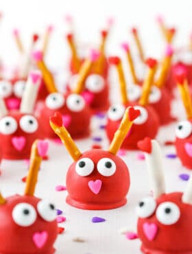 Love Bug Oreo Cookie Balls with pretzel sticks for feelers and heart noses displayed on a white marble table top