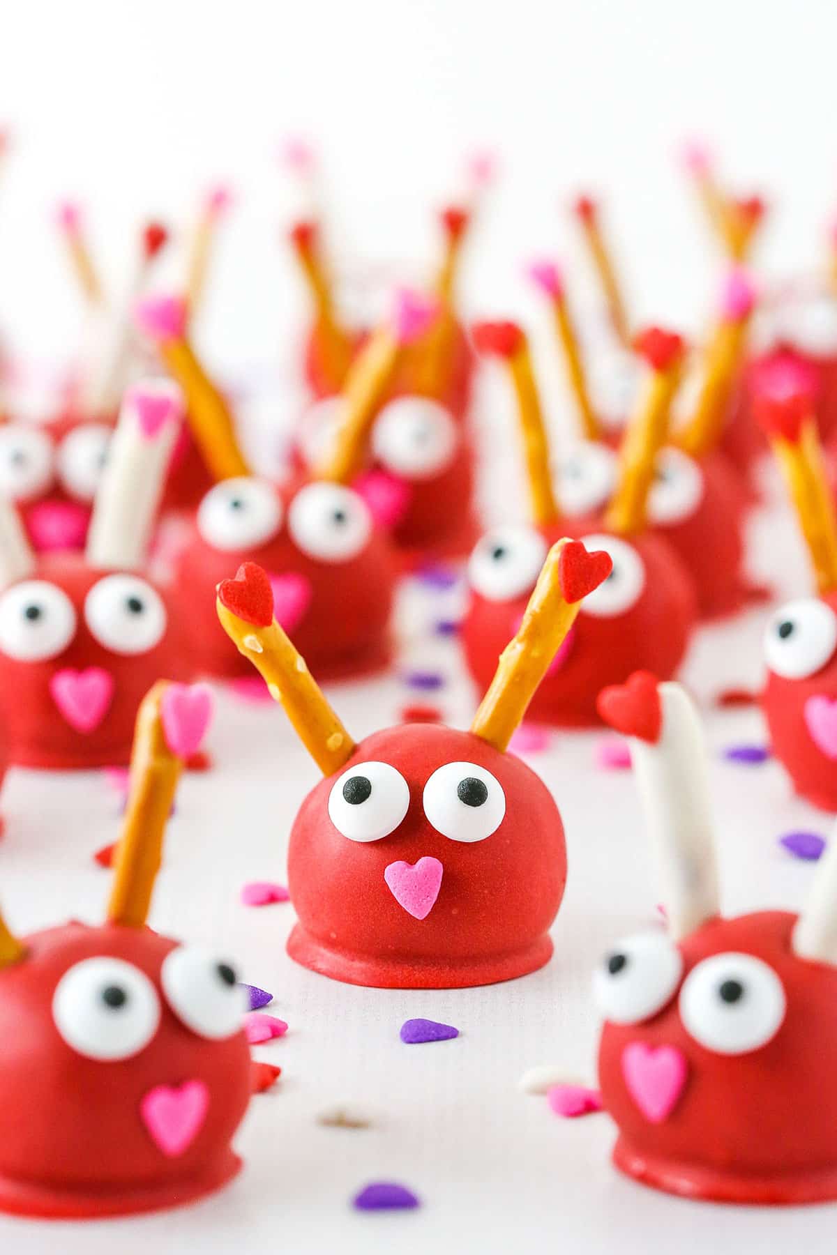 Love Bug Oreo Cookie Balls with pretzel sticks for feelers and heart noses displayed on a white marble table top