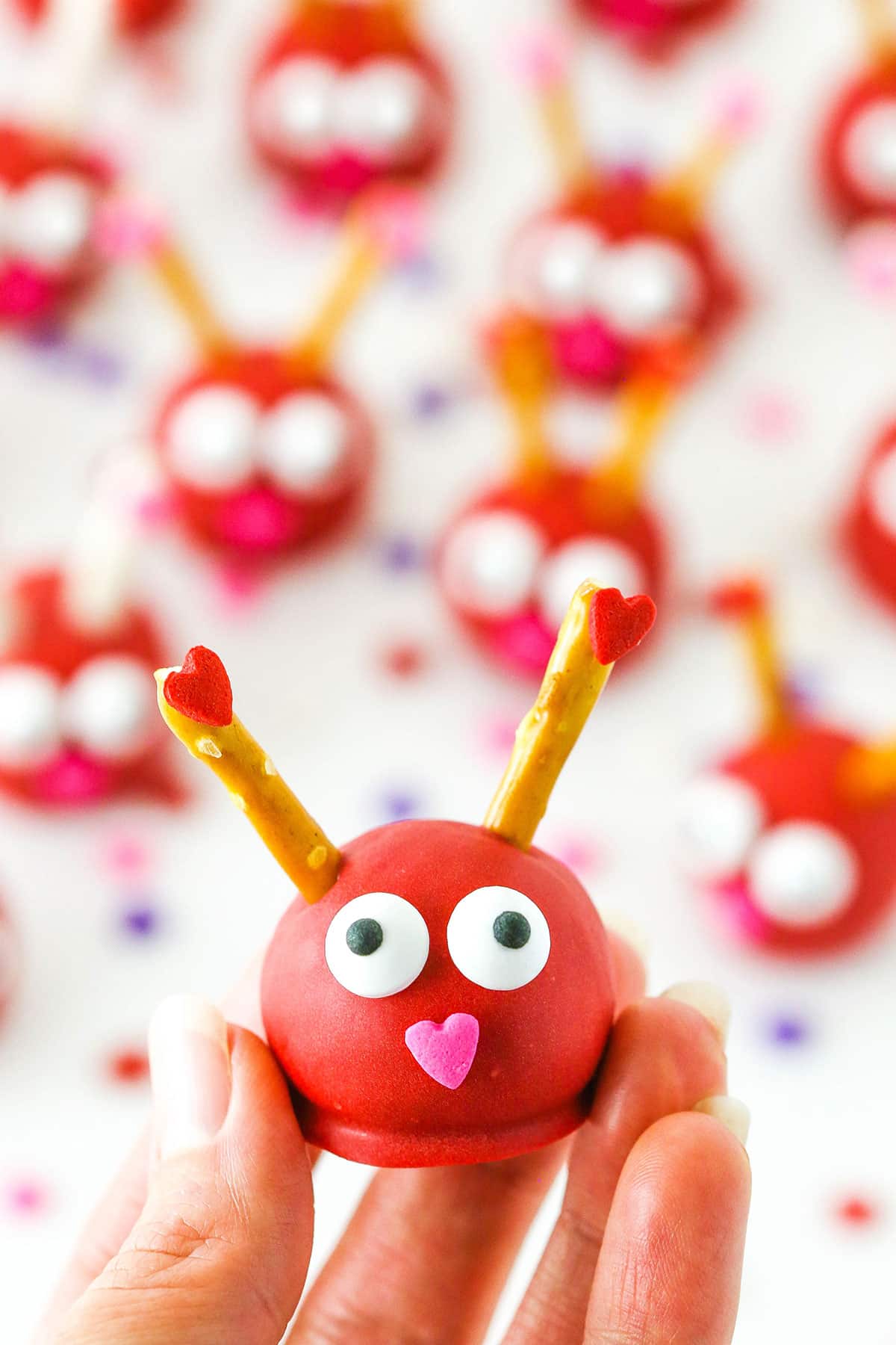 Love Bug Oreo Cookie Balls with pretzel sticks for feelers and heart noses displayed on a white marble table top