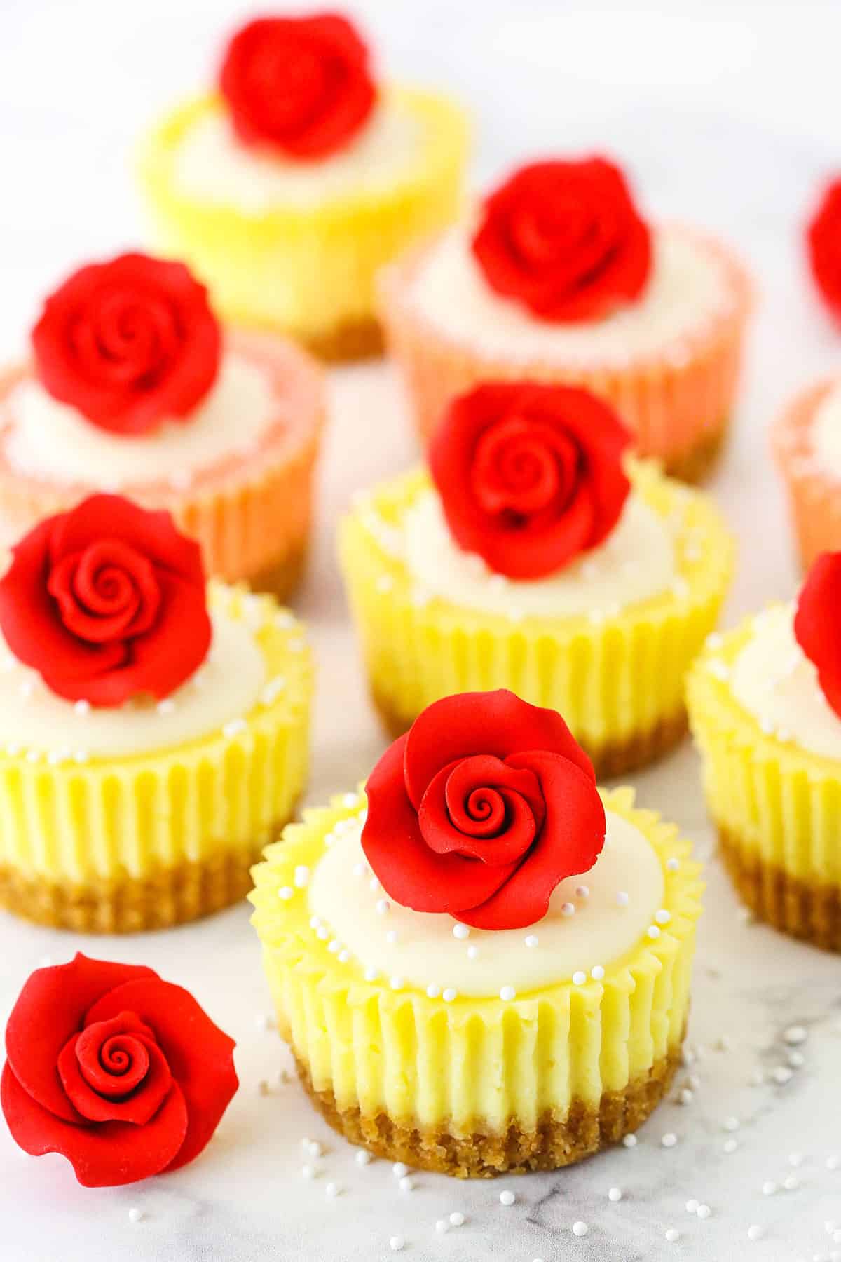 Mini Rose Cheesecakes topped with white icing and a red rose on a white marble table