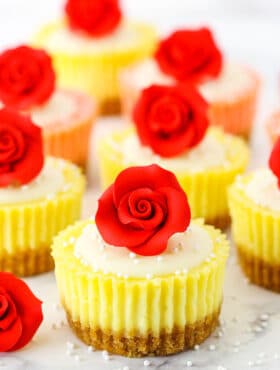 Mini Rose Cheesecakes topped with white icing and a red rose on a white marble table