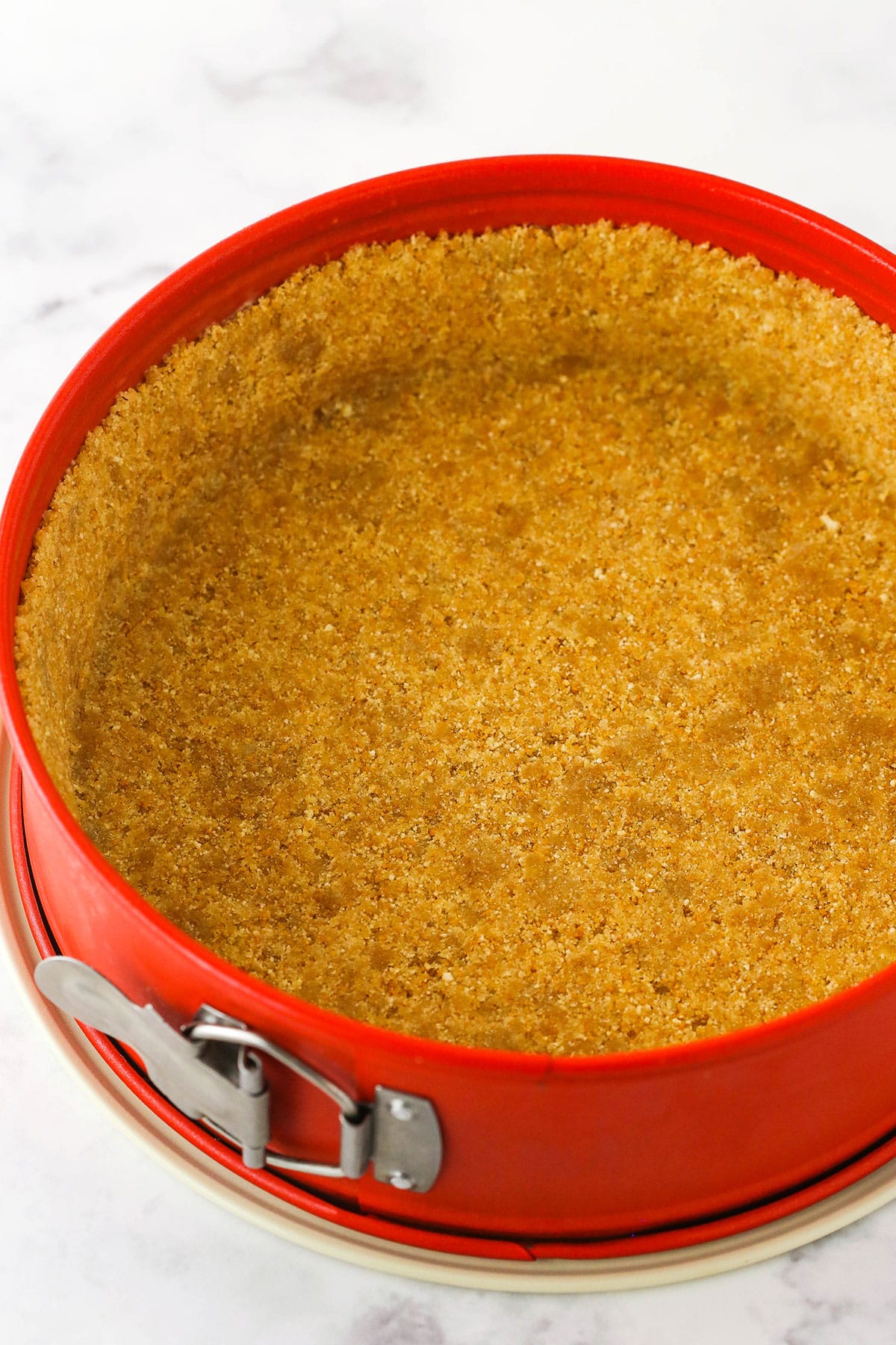 A step in making No Bake Cherry Almond Cheesecake showing the prepared crust being pressed into the bottom and sides of a springform pan.