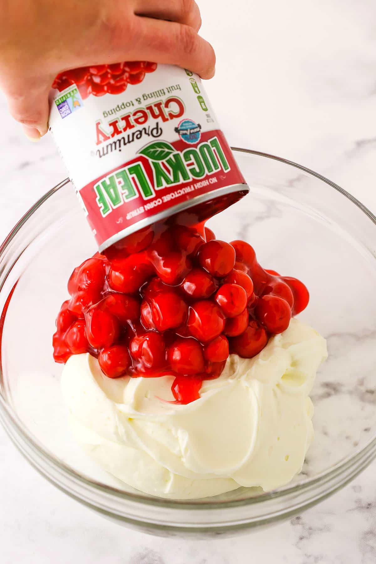 A step in making No Bake Cherry Almond Cheesecake showing adding a full can of Lucky Leaf Cherry Fruit Filling to the cheesecake filling