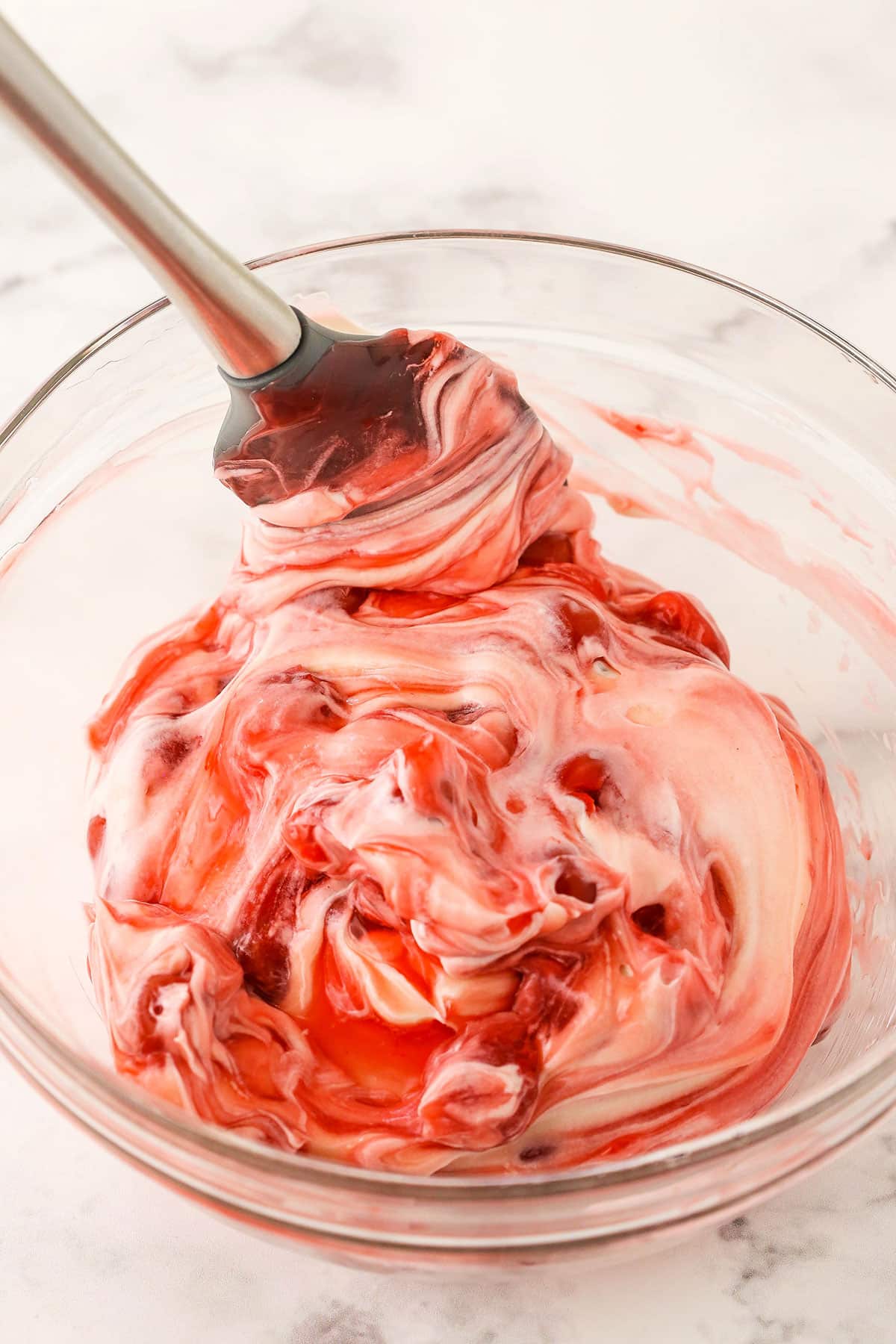 A step in making No Bake Cherry Almond Cheesecake showing folding the added fruit into the cheesecake filling using a spatula.