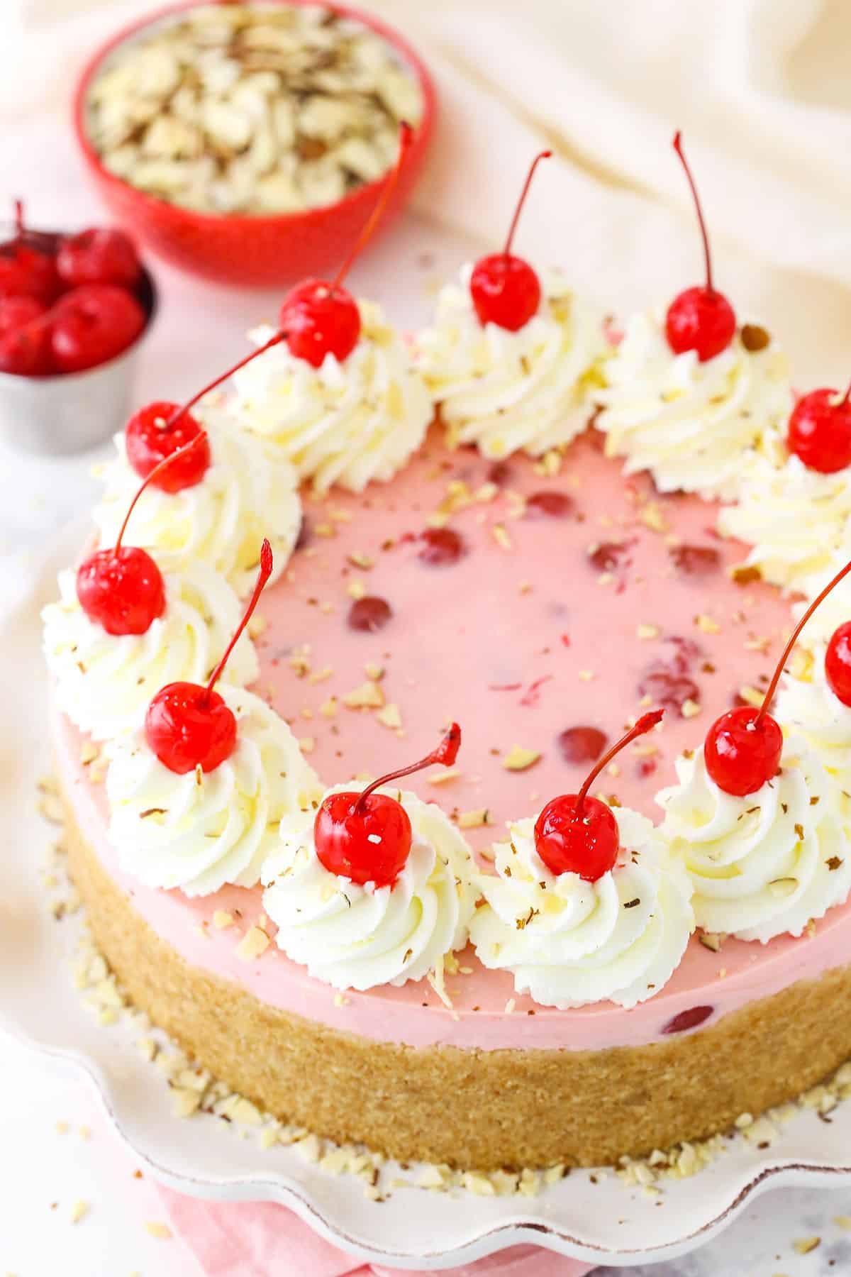 Overhead view of a full No Bake Cherry Almond Cheesecake topped with white swirls and cherries on a white platter