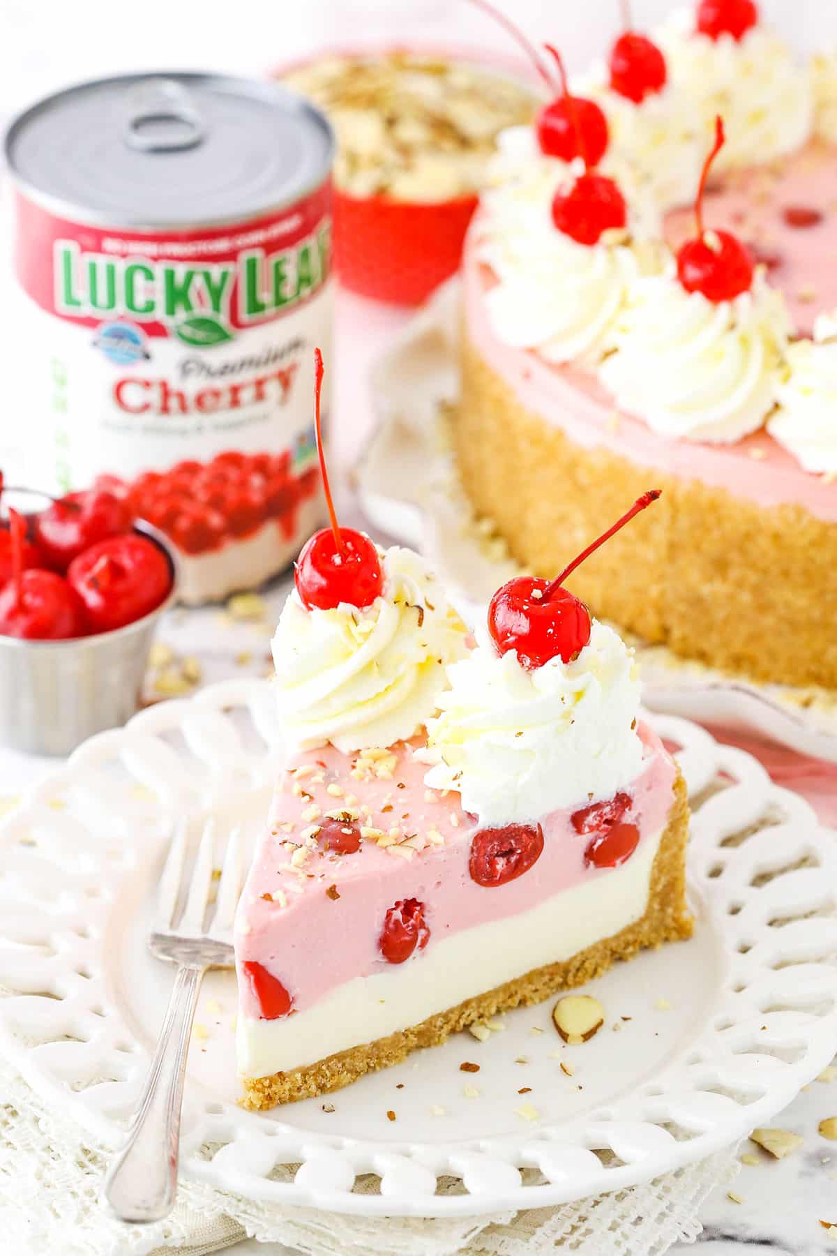 A slice of No Bake Cherry Almond Cheesecake topped with white swirls and cherries on a white plate with a fork