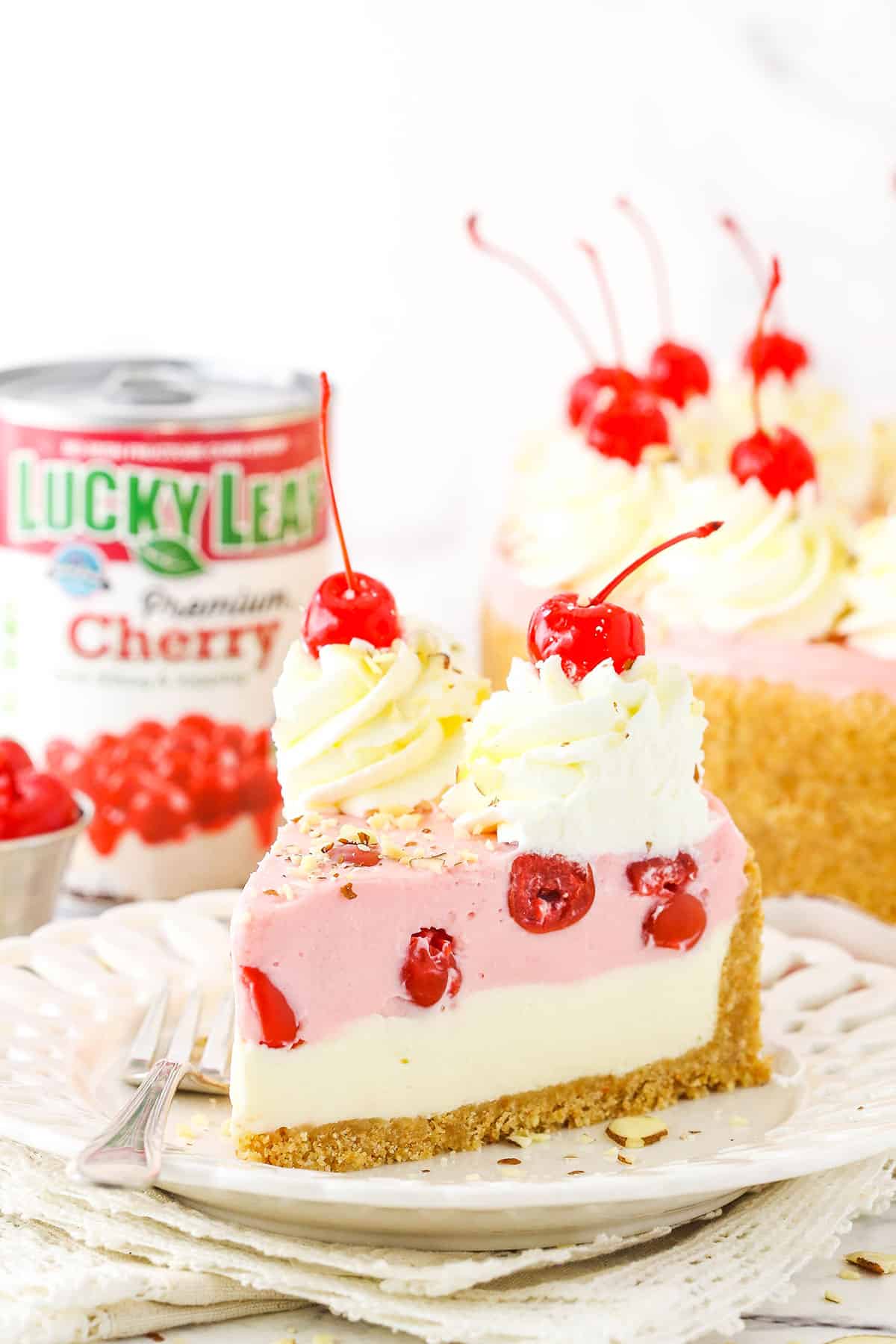 A slice of No Bake Cherry Almond Cheesecake topped with white swirls and cherries on a white plate with a fork