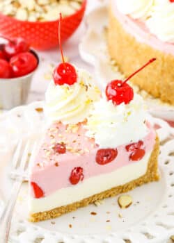 A slice of No Bake Cherry Almond Cheesecake topped with white swirls and cherries on a white plate with a fork