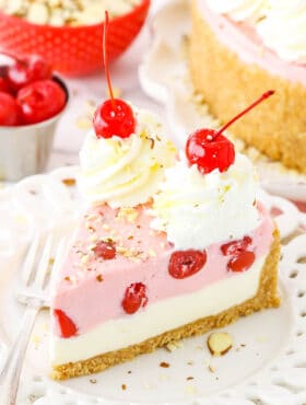 A slice of No Bake Cherry Almond Cheesecake topped with white swirls and cherries on a white plate with a fork