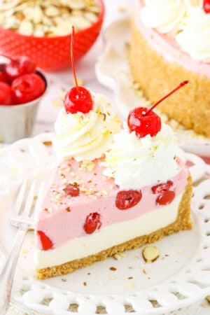 A slice of No Bake Cherry Almond Cheesecake topped with white swirls and cherries on a white plate with a fork