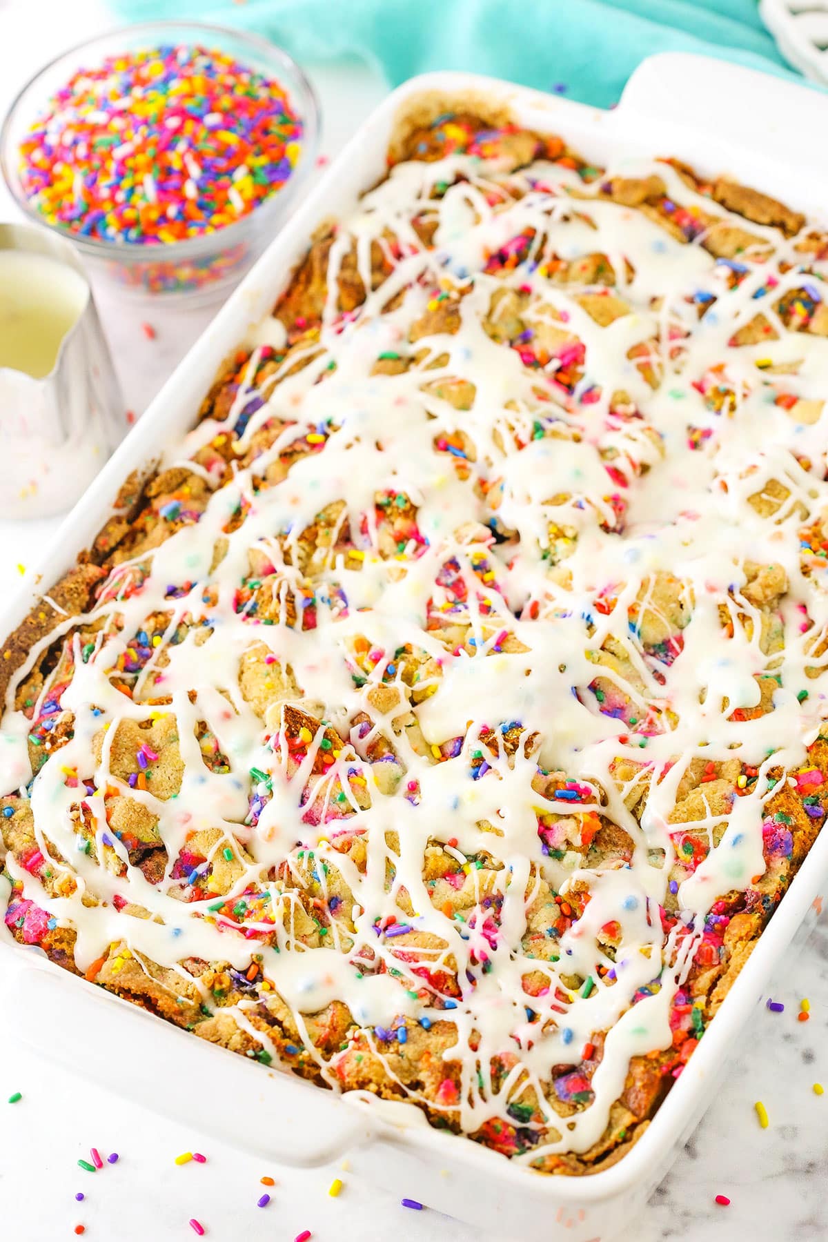 This Overnight Birthday Cake French Toast Casserole is the perfect breakfast for a birthday or special occasion! Prepare this breakfast casserole the night before and wake up to a delicious party in a pan! Overhead view of Overnight Birthday Cake French Toast Casserole topped with colorful sprinkles and icing in a white platter