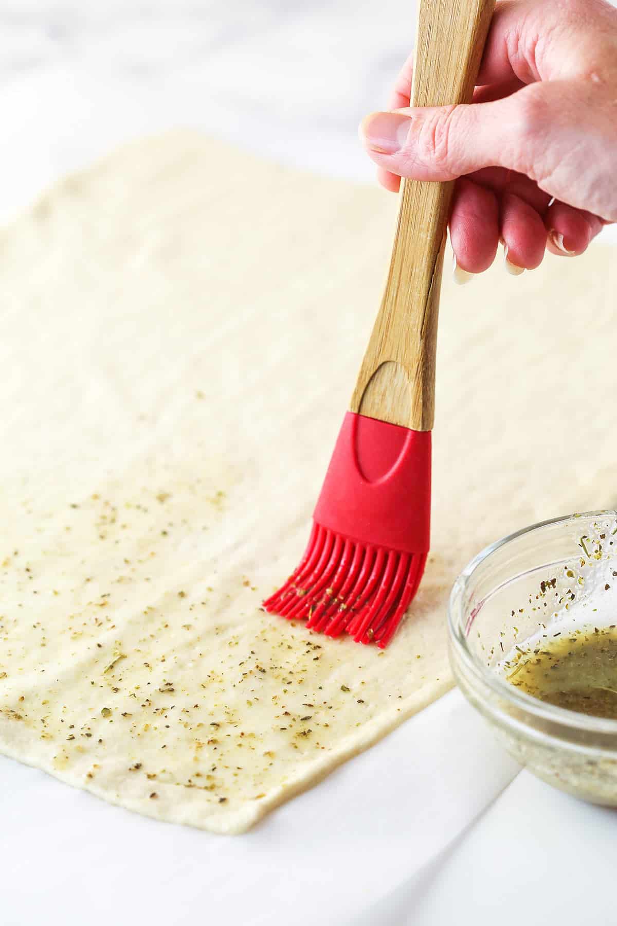 Brushing pizza dough with seasoned butter.