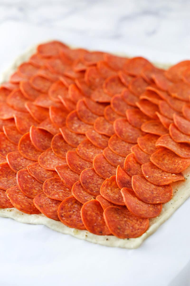 Pepperoni rolls are made up of pizza dough brushed with butter, wrapped around pepperoni and mozzarella cheese, and baked to golden brown. Arranging pepperoni on top of pizza dough.