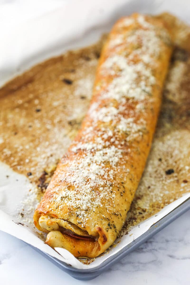 A baked, unsliced pepperoni roll on a baking sheet lined with parchment paper.