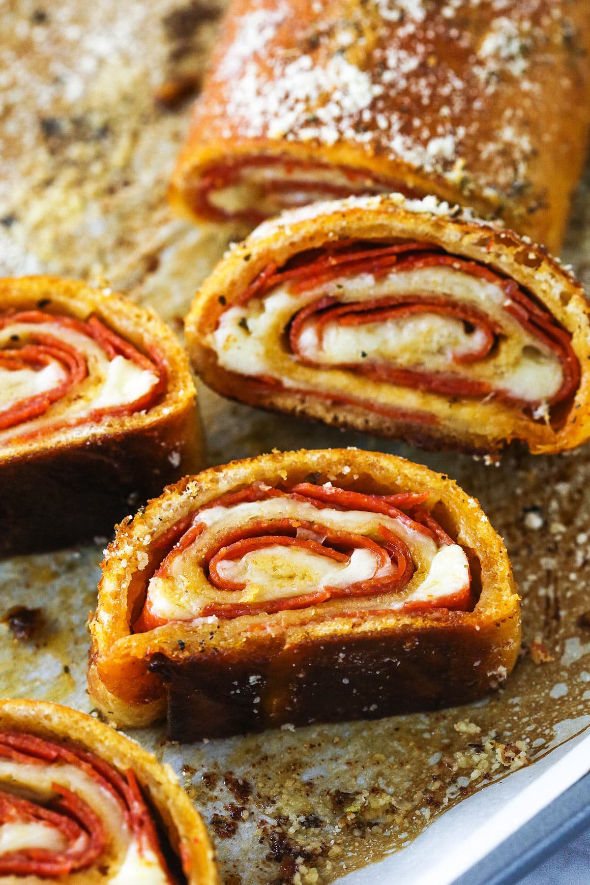 Pepperoni rolls are made up of pizza dough brushed with butter, wrapped around pepperoni and mozzarella cheese, and baked to golden brown. Closeup of a full pepperoni roll with slices of pepperoni roll.