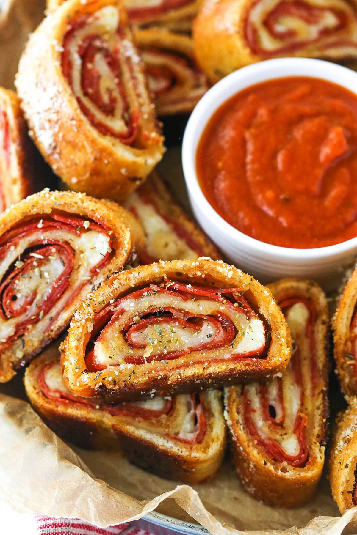 Closeup of pepperoni rolls with marinara sauce on a serving tray lined with parchment paper.