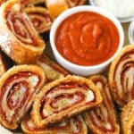 Closeup of pepperoni rolls with marinara sauce and parmesan cheese on a serving tray lined with parchment paper.