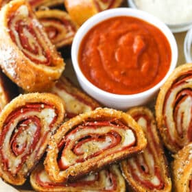 Closeup of pepperoni rolls with marinara sauce and parmesan cheese on a serving tray lined with parchment paper.
