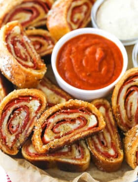 Closeup of pepperoni rolls with marinara sauce and parmesan cheese on a serving tray lined with parchment paper.