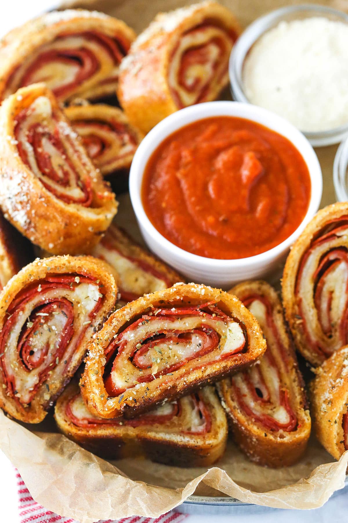 Closeup of pepperoni rolls with marinara sauce and parmesan cheese on a serving tray lined with parchment paper.