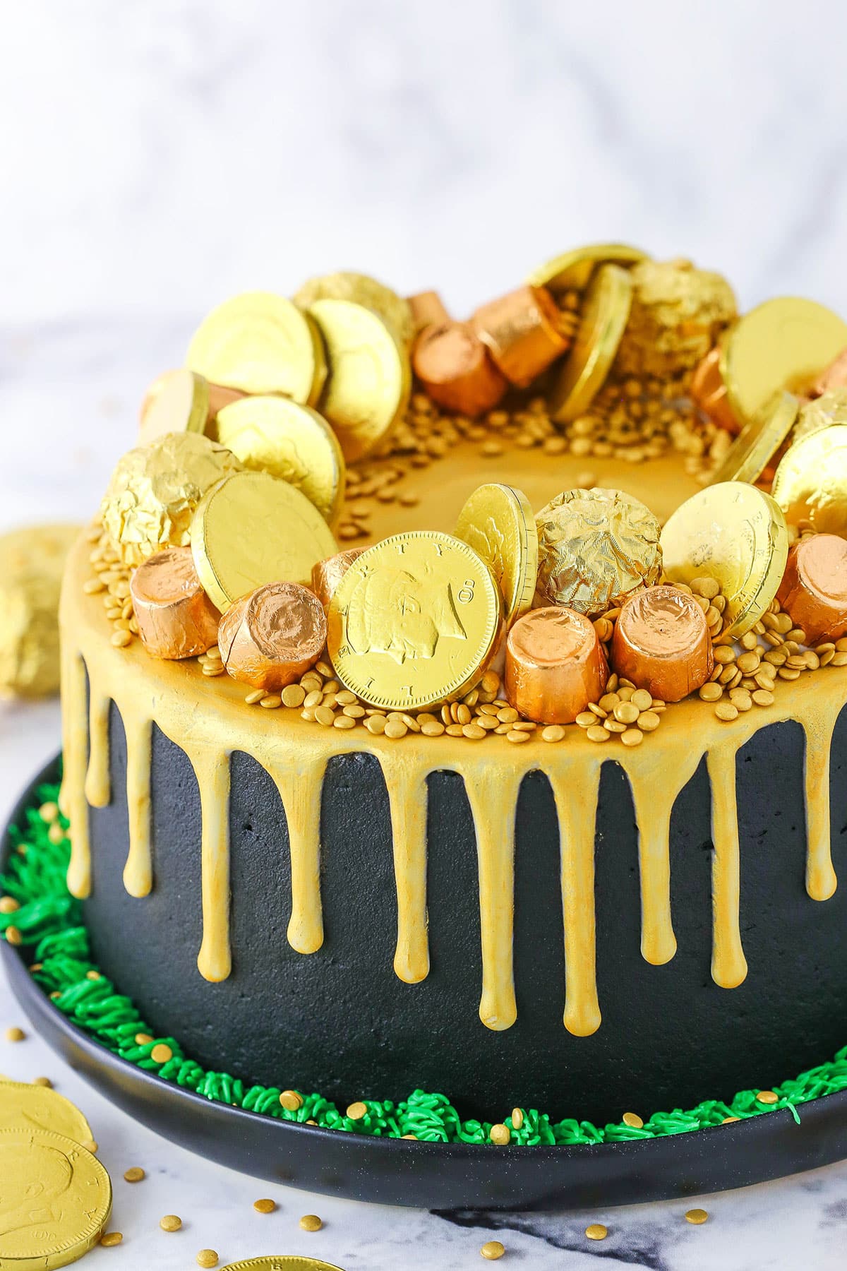 Side view of a full Pot Of Gold Cake decorated with gold wrapped chocolate coins and gold drip in a black pan