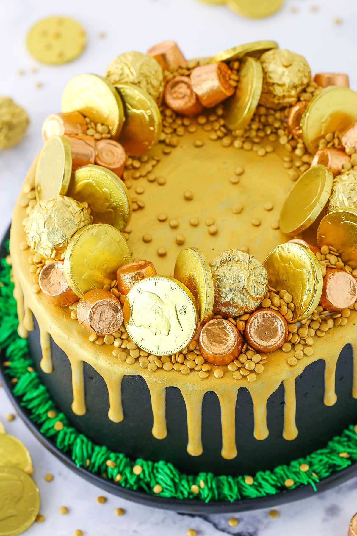 This Pot of Gold Cake is such a fun cake for St. Patrick's Day! Lots of chocolate and all the "gold" you could want! Cut into it and see all the "gold" fall out! Overhead view of a full Pot Of Gold Cake decorated with gold wrapped chocolate coins and gold drip in a black pan