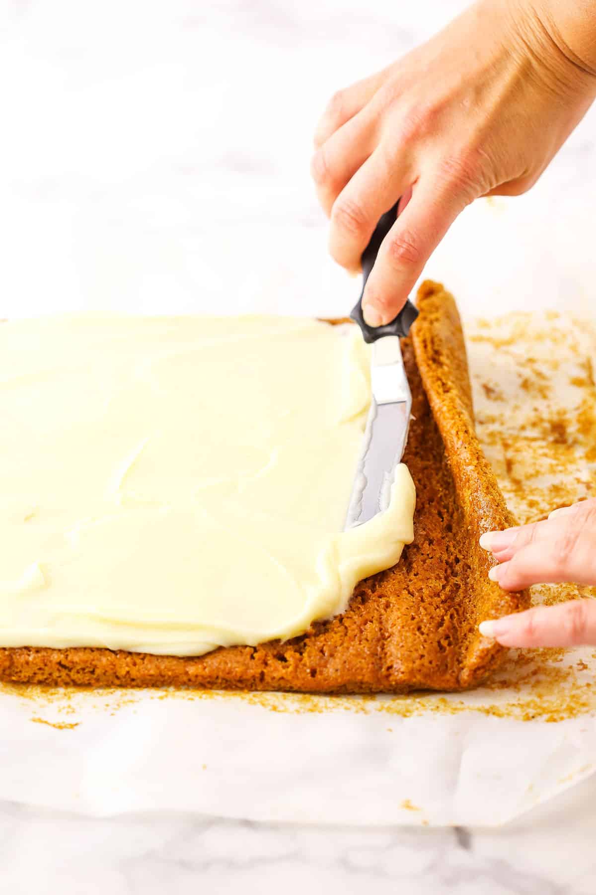 A step in making Pumpkin Roll Cake showing the filling being spread evenly over the cooled cake using an offset spatula