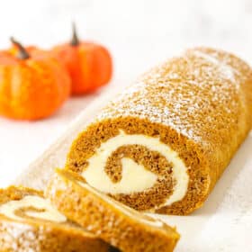 Two slices of Pumpkin Roll Cake layered in front of the rest of the Pumpkin Roll Cake on a white platter