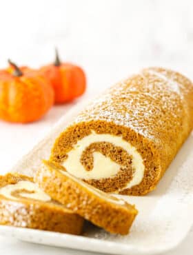 Two slices of Pumpkin Roll Cake layered in front of the rest of the Pumpkin Roll Cake on a white platter