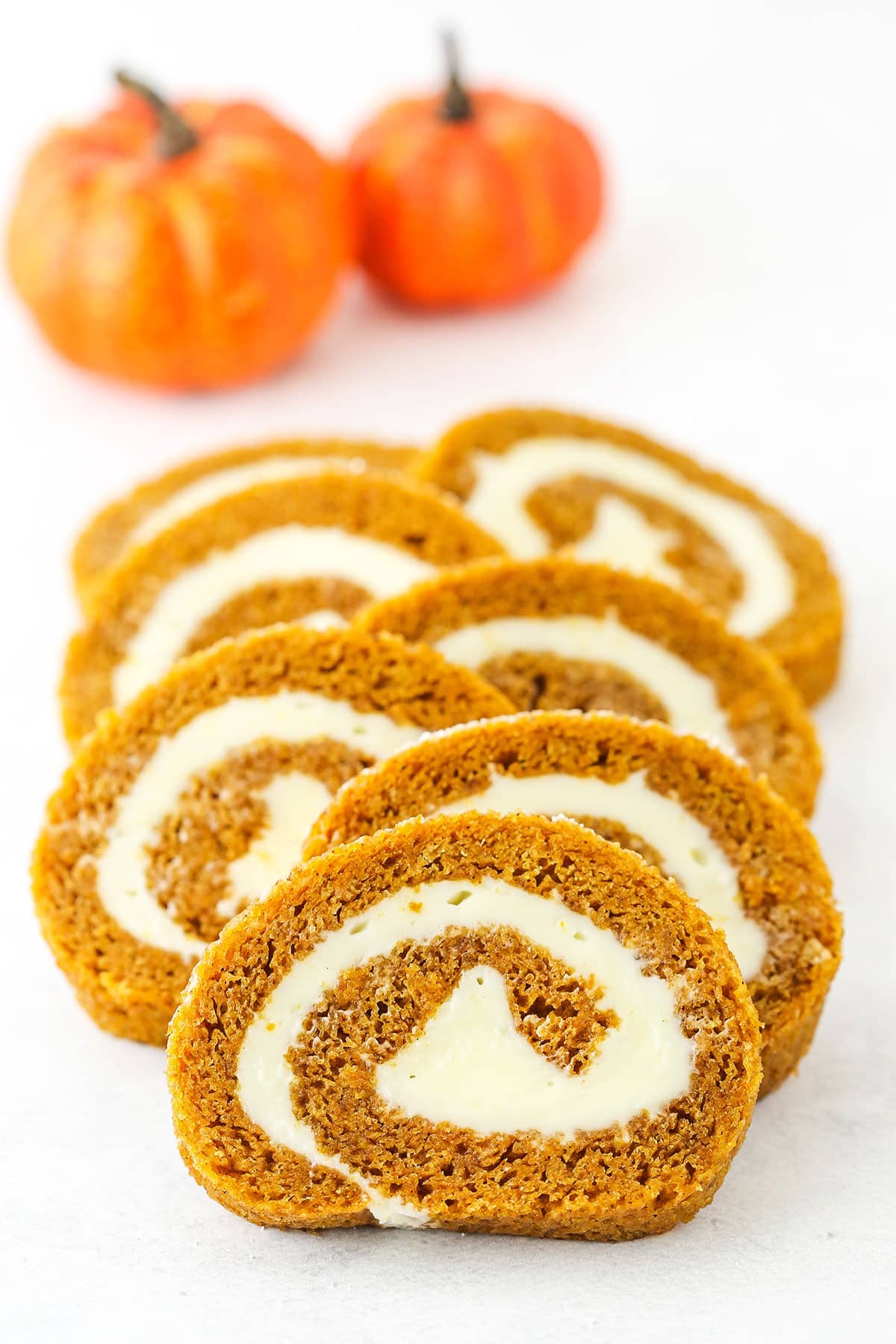 Seven slices of Pumpkin Roll Cake overlapping each other on a white table top.