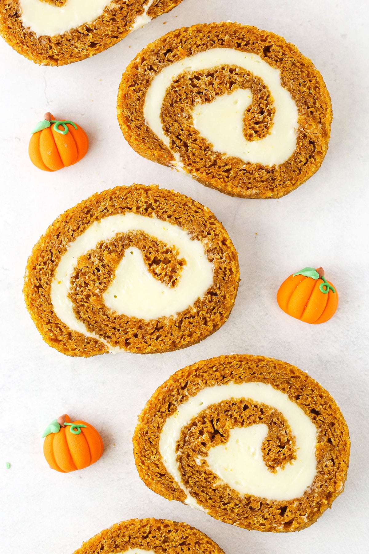 Overhead view of five slices of Pumpkin Roll Cake spread out on a white table with three pumpkin shaped candies.