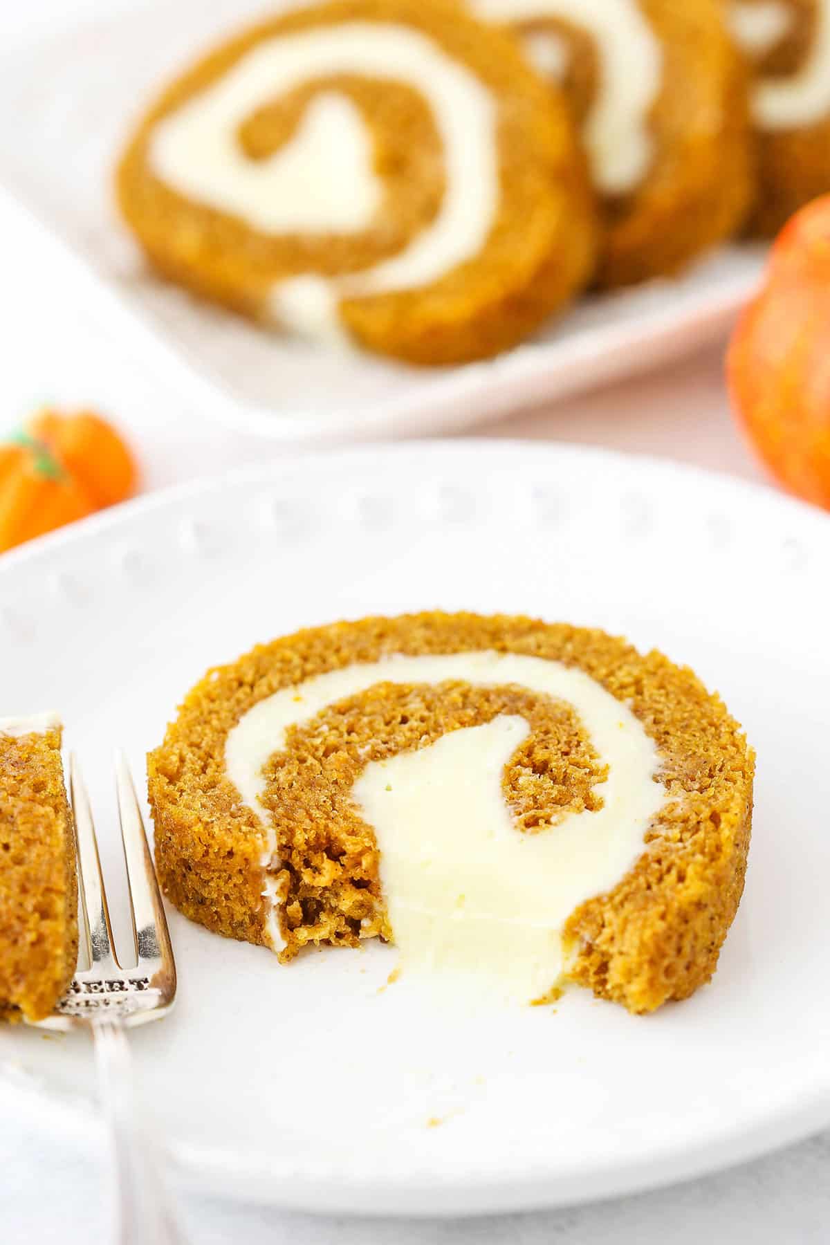 A slice of Pumpkin Roll Cake with a bite removed on a white plate next to a fork.