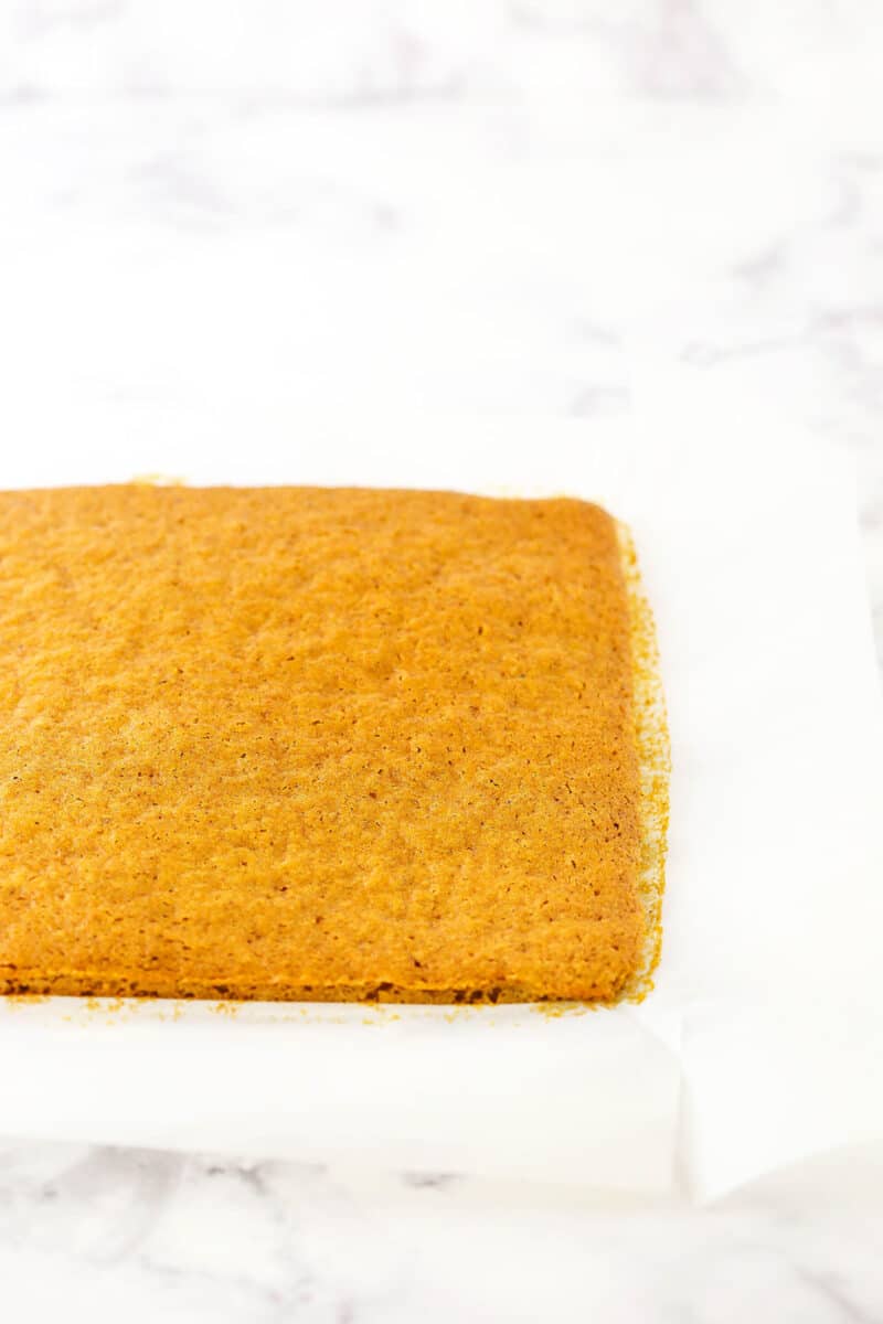 Pumpkin cake being rolled in parchment paper.