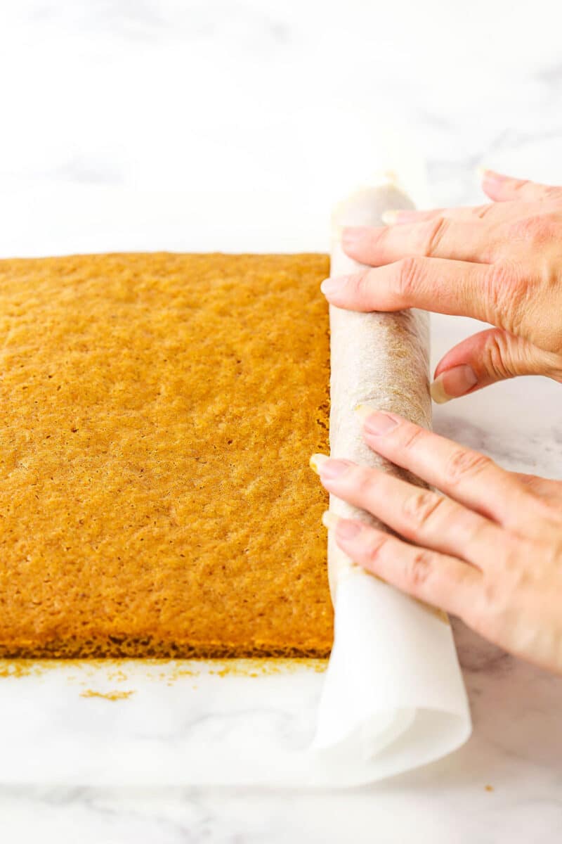 A step in making Pumpkin Roll Cake showing rolling the cake on the parchment paper and forming the shape of the cake.