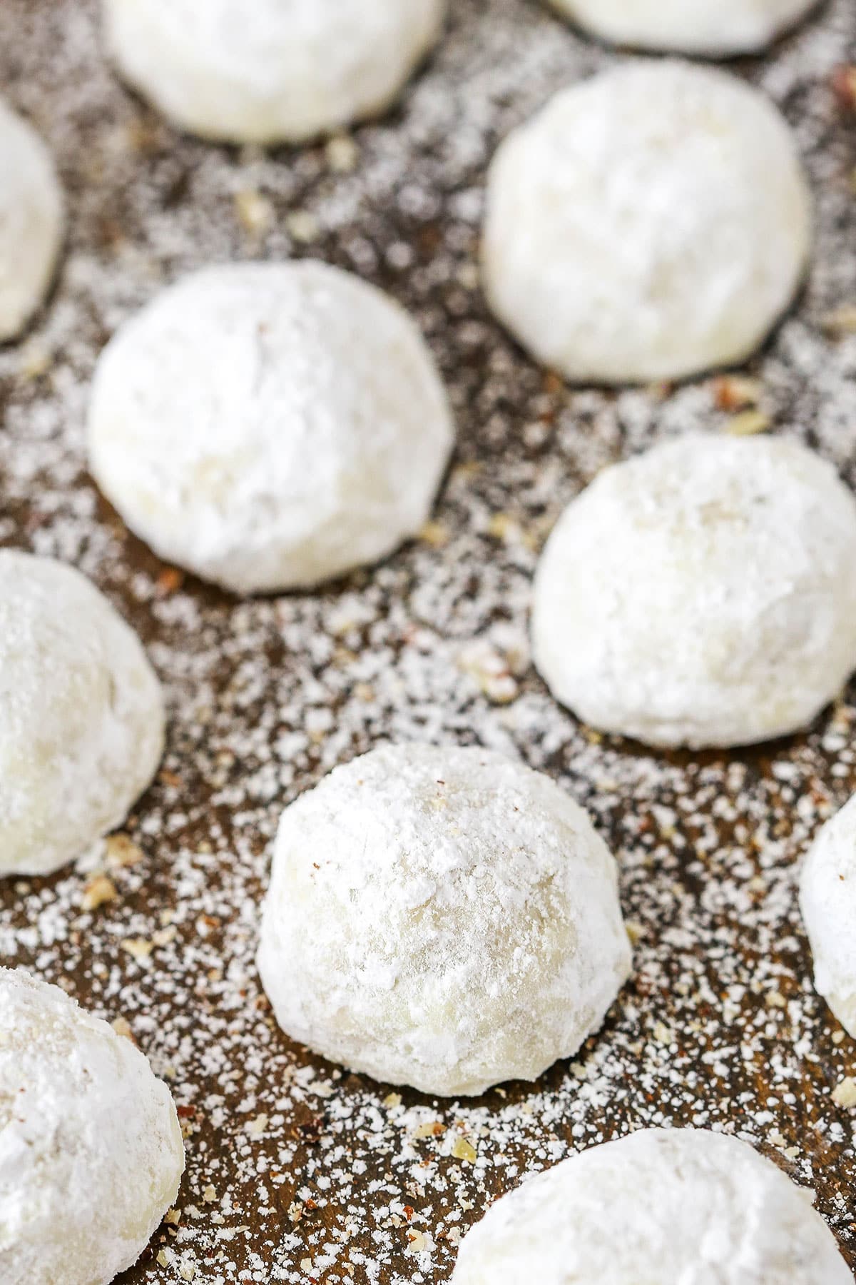 Russian Tea Cakes spread out evenly on a wooden board and coated in powdered sugar